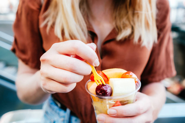 sliced fruits on a take away plastic cup. It is hold by an unrecognizable blonde woman - Foto, Imagem