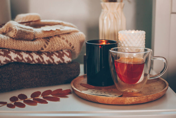 Still life details. Cup of tea and candles on wooden tray and stack of warm woolen sweaters. Autumn mood, cozy home, hygge concept - Fotografie, Obrázek