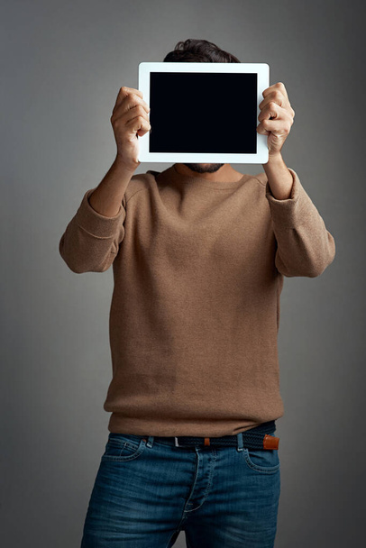 Can I draw your attention to this. Studio shot of a man covering his face with a blank digital tablet against a gray background - Foto, imagen