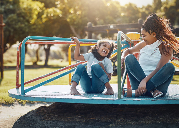 Enjoying some quality time out in the lovely sunshine. a mother and her daughter playing together on a merry-go-round at the park - Foto, immagini