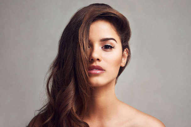 Beauty is flowing hair and glowing skin. Studio shot of a young beautiful woman with long gorgeous hair posing against a grey background - Photo, image
