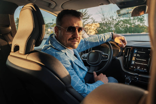 Portrait of stylish business man with sunglasses looking at camera inside his expensive automobile. - Foto, Bild