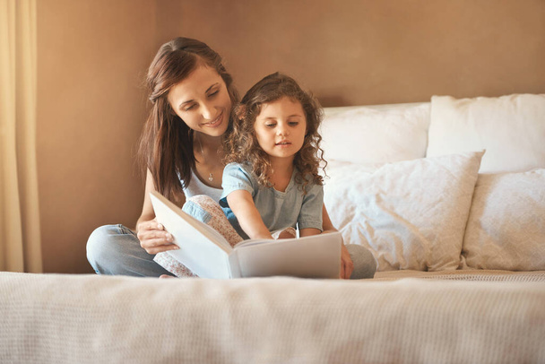 Please read it again mommy. a happy mother and daughter at home reading a storybook on the bed - Фото, зображення