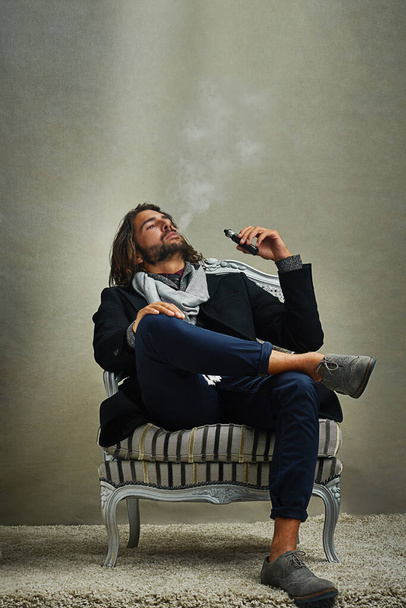 Smoking never looked this cool. a stylishly dressed man smoking an electronic cigarette while sitting in the studio - Foto, imagen
