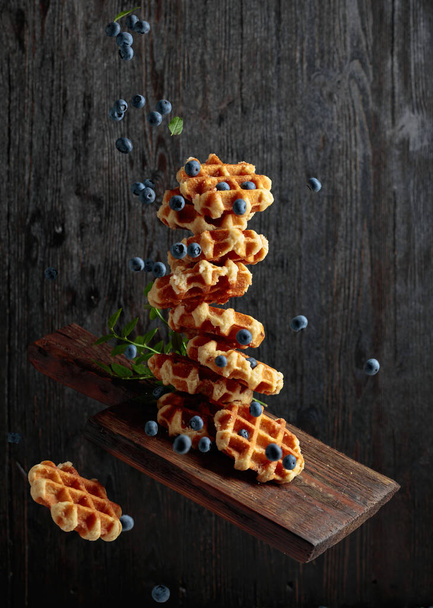 Waffles with fresh blueberries in motion on a black wooden background. - Foto, imagen