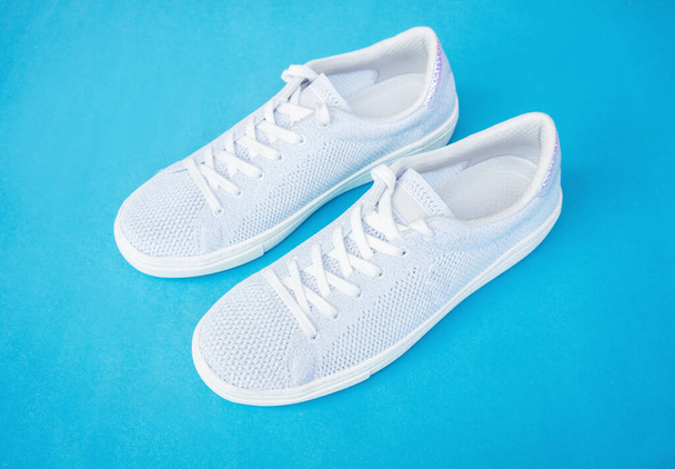 Pair of white female fashion sneakers on blue background.Top view. - Photo, Image