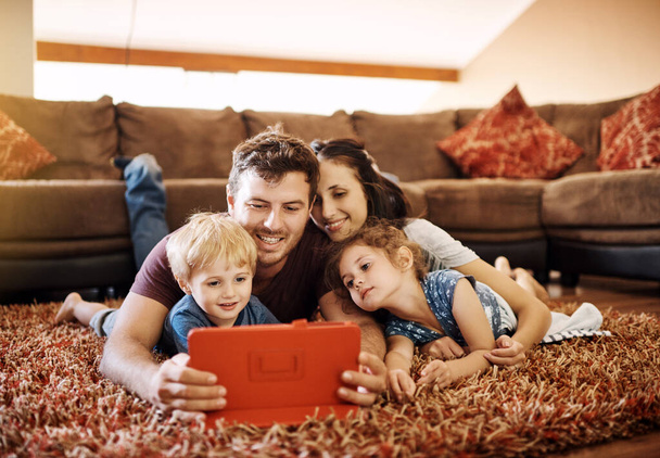 Technology keeps everyone entertained. a happy young family looking at a tablet together while lying on the carpet in their lounge - Φωτογραφία, εικόνα
