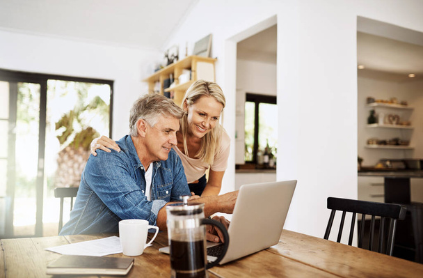 Couple with laptop planning finance, banking and checking retirement budget while becoming debt free at home. Smiling, happy and cheerful mature man showing woman an approved bank loan on technology. - Φωτογραφία, εικόνα