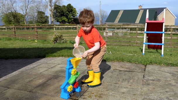 Red headed boy having fun playing with water in the garden - Photo, Image
