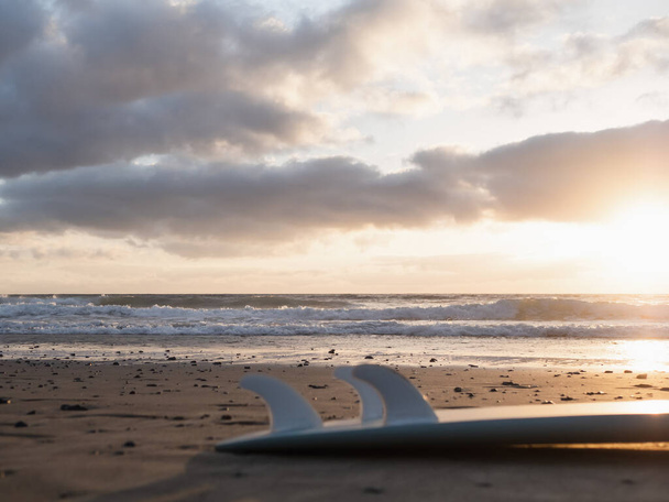Morning waves at sunrise and a surfboard lying on the beach - Fotoğraf, Görsel