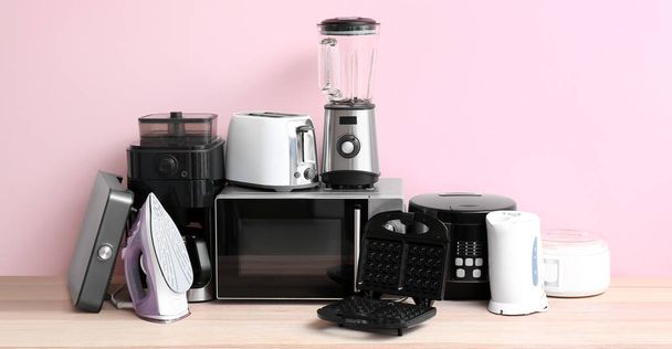 Different household appliances on table against pink background  - Foto, Imagem