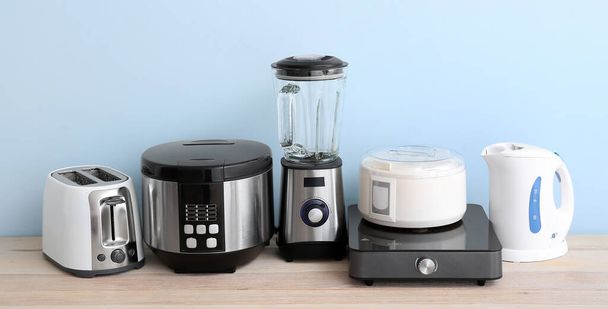 Different household appliances on table against light blue background  - Foto, Bild