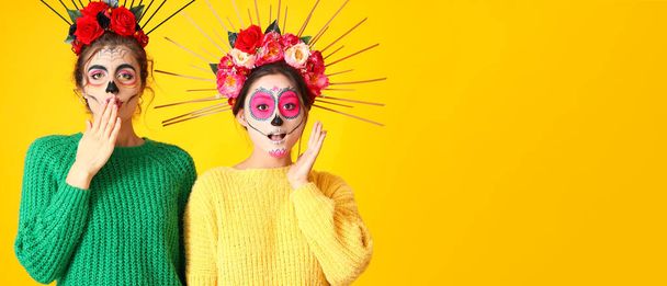 Surprised women with painted skull on faces against yellow background with space for text. Halloween celebration - 写真・画像
