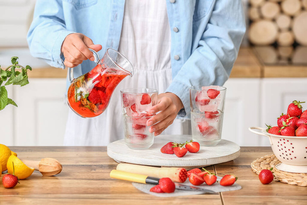 Woman pouring tasty strawberry lemonade into glass in kitchen - Fotoğraf, Görsel