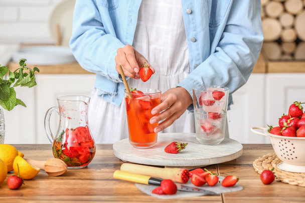 Woman putting strawberry into glass of lemonade on table - Foto, afbeelding