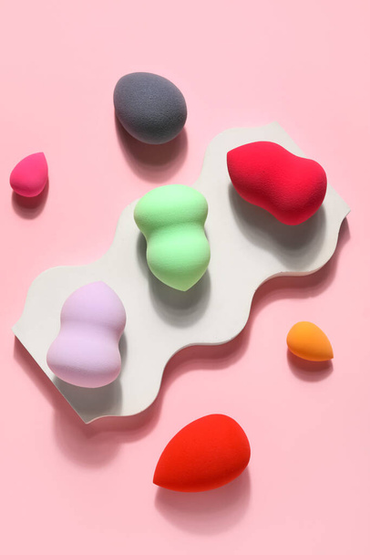 Stand with colorful makeup sponges on pink background - 写真・画像