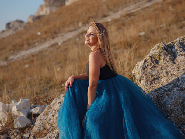 Fashionable woman on desert field near mountain wearing black top and blue tulle skirt. Wild west. Summer holidays dance. Beautiful and sexy plus size model - Foto, Imagen