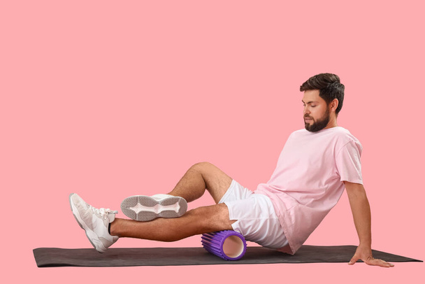 Young man training with foam roller on pink background - Foto, Imagem