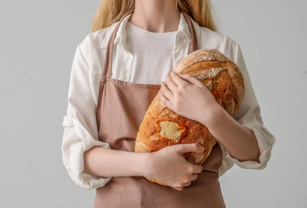 Young woman with fresh bread on light background, closeup - Фото, зображення