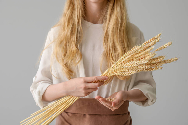 Young woman with wheat ears on light background, closeup - Foto, Imagen