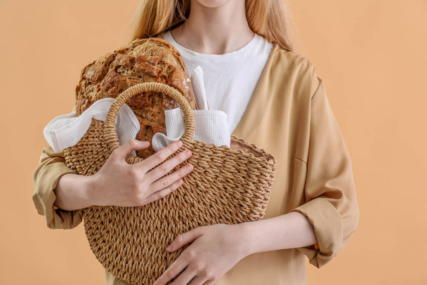 Νεαρή γυναίκα κρατώντας τσάντα με φρέσκο ψωμί σε μπεζ φόντο - Φωτογραφία, εικόνα