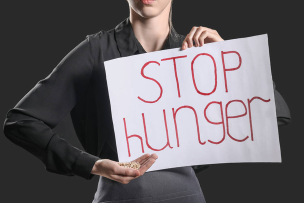 Young woman holding paper with text STOP HUNGER on black background - Foto, Imagem