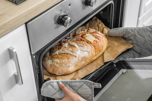 Woman taking baking sheet with bread from oven in kitchen, closeup - Fotoğraf, Görsel