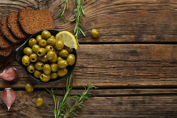 Состав с миской вкусных зеленых оливок, хлеба и специй на деревянном фоне - Фото, изображение