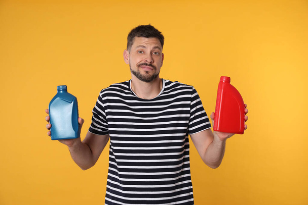 Confused man holding two containers of motor oil on orange background - Photo, image
