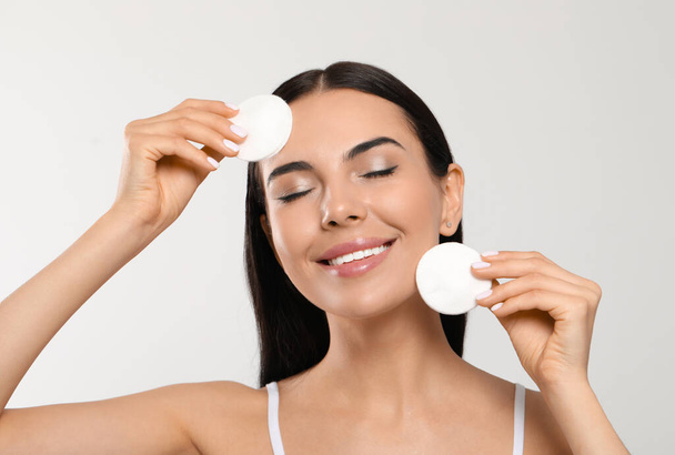 Young woman using cotton pads with micellar water on light grey background - Фото, зображення