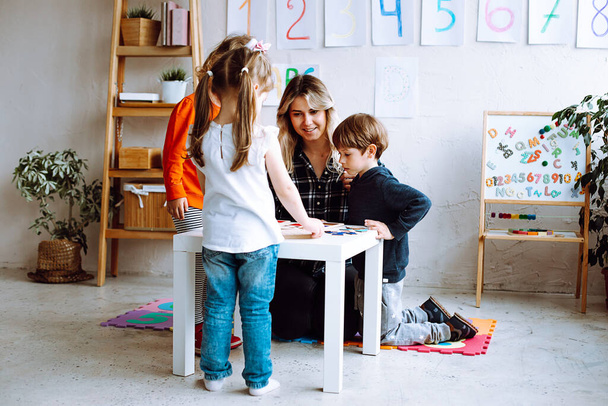 Group of amazing children studying with help of teacher woman in bright classroom. Pupils learning board games near magnetic board with alphabet, numbers. Early development, preschool education. - Photo, image