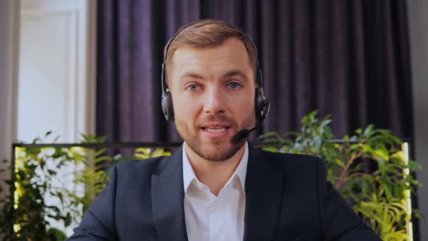 Business video call, handsome customer support operator assistant working at helpdesk with a headset online from remote workplace technical support internet communication headphones microphone - Imágenes, Vídeo