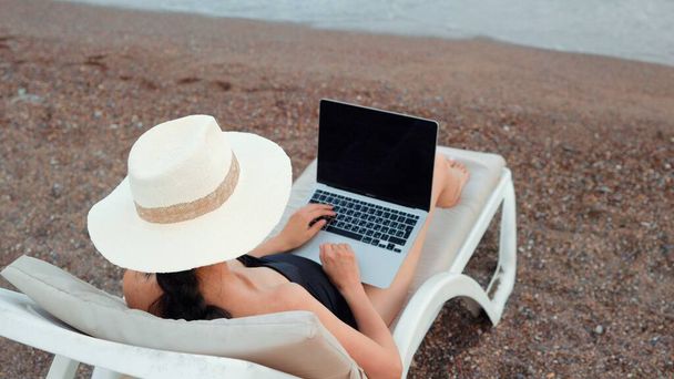 Вид сзади на женщину-фрилансера, работающую на ноутбуке у моря. Концепция удаленной работы. работа в отпуске. Высококачественные 4k кадры - Фото, изображение