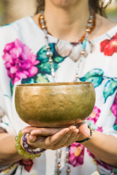 Detail of a woman's hands holding a Tibetan singing bowl during a meditation and music therapy session in a park area. - Photo, image