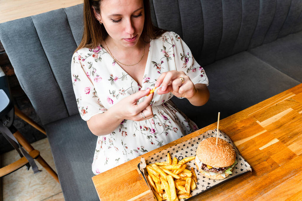 Бургер беременная девушка ест. Голодная беременная женщина ест вкусный гамбургер. Концепция нездорового питания - Фото, изображение