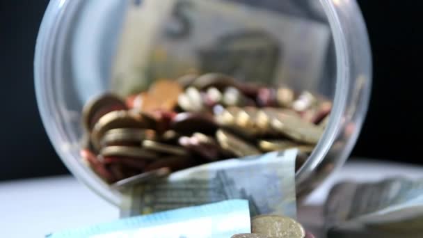 Euro money savings sliding inside glass jar full of Euro coins and Euro banknotes for financial management of pocket money and tip or gratuity for piggy bank currency pile as cash close-up macro view - Materiał filmowy, wideo