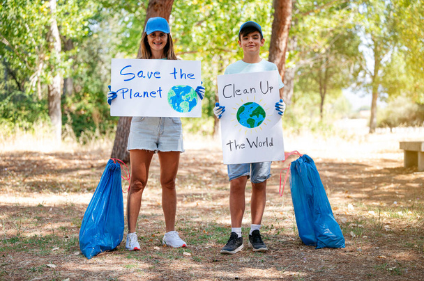 Женщины и дети-волонтеры собирают мусор и держат в руках знак "Очистить мир" и спасают планету в парке - Фото, изображение