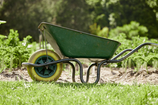 Farm or garden wheelbarrow on nature, agriculture environment or green countryside field used for farming work. Gardening equipment for lawn with sustainable grass, flower and plant growth. - Foto, immagini
