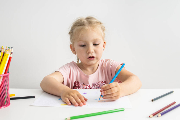 Blonde child girl draws with colored pencils sitting at the table. - Foto, afbeelding