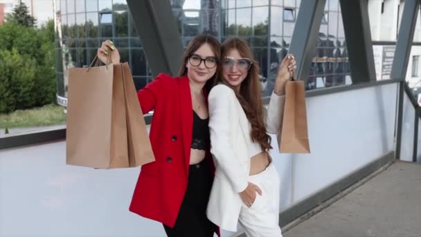 Две счастливые женщины в стильных костюмах стоят вместе перед торговым центром с большим количеством бумажных пакетов.. - Кадры, видео