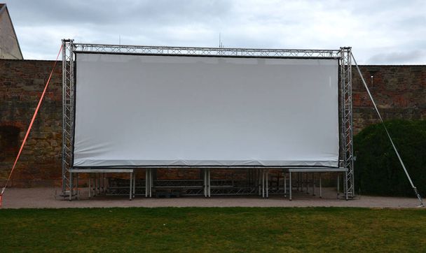 αλουμινένια κατασκευή σκηνής. μεγάλη οθόνη λευκό, μουσαμά, υπαίθριο κινηματογράφο στο πάρκο. ασφαλισμένο με κορδόνια. μια βραδινή προβολή κάτω από τον ουρανό έχει συσταθεί στο πάρκο - Φωτογραφία, εικόνα