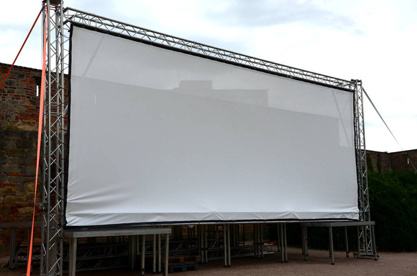 aluminum stage construction. large format white screen, tarpaulin, outdoor cinema in the park. secured with drawstrings. an evening screening under the sky is set up in the park - Foto, Imagen