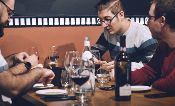 Μια ομάδα αρρένων φίλων κάθισε σε ένα τραπέζι απολαμβάνοντας ένα γεύμα σε ένα εστιατόριο - Φωτογραφία, εικόνα