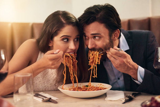 Это гонка до финиша. молодая пара делит тарелку спагетти во время романтического ужина в ресторане - Фото, изображение