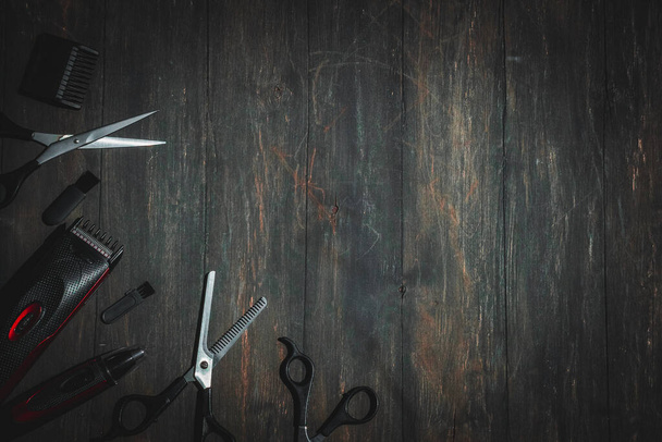Scissors, combs, shampoo and men's hair clipper lie on the left on a black wooden background with copy space on the right, flat lay close-up. The concept of a male barbershop. - Photo, image