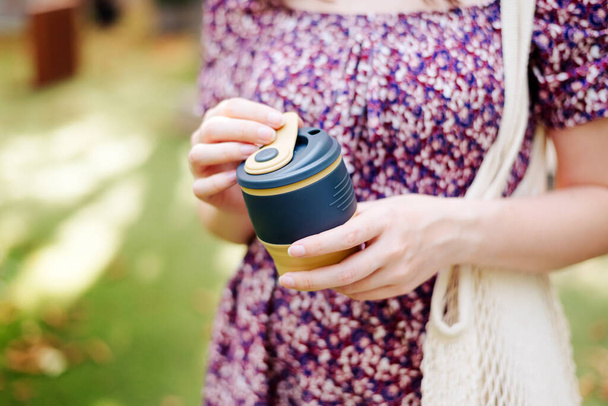 Young female in dress holding reusable silicone foldable coffee tea mug close-up. eco-friendly. mesh cotton bag. - Photo, image