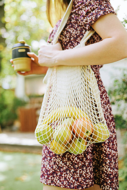 Женская рука со свежими фруктами в бежевом вязаном пакете. Нулевые отходы, концепция здорового питания - Фото, изображение