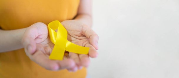 Młoda kobieta z żółtą złotą wstążką symbolem świadomości endometriozy, zapobiegania samobójstwom, raka kości mięsaka, raka pęcherza moczowego, raka wątroby i koncepcji raka z dzieciństwa. Opieka zdrowotna. Przestrzeń kopiowania. - Zdjęcie, obraz
