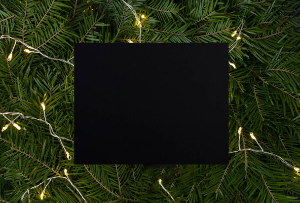 Рождественский фон Крупный план еловых ветвей с светящимися гирляндами и пустой черной карточкой для текста. Копирование пространства. - Фото, изображение