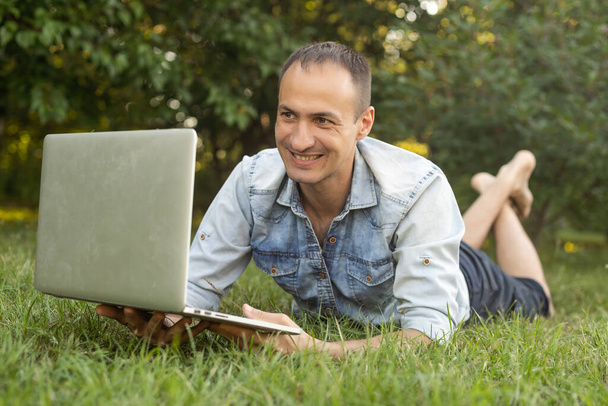 夏の庭の若い男は、ラップトップコンピュータでオンラインでフリーランサーとしてチャットしながら - 写真・画像